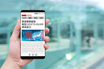 緊急事態宣言のニュースを表示するスマホを持つ男性の手と街並み背景