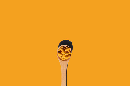 Wooden Spoon With Turmeric Curcumin Capsules On Yellow Background