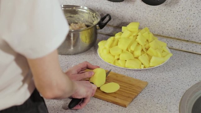 hands cut potatoes in slices on wooden board