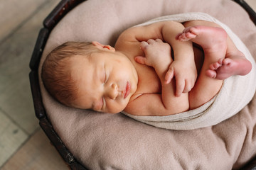 Newborn baby boy, in the photo the baby is 7 days old from birth, wrapped in a wrapping, sleeps sweetly in a basket