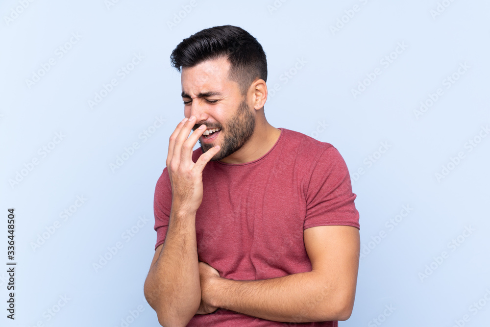 Wall mural Young handsome man with beard over isolated blue background smiling a lot