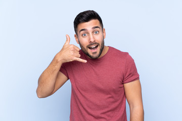 Fototapeta premium Young handsome man with beard over isolated blue background making phone gesture. Call me back sign