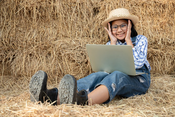 Naklejka na ściany i meble Young girl wear glasses and using a notebook to study agriculture with relax on a haystack in the barn. She has the idea of ​​farming and expanding her father's career as a farmer. Light and shadow.