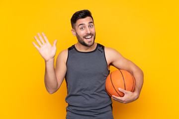 Handsome young basketball player man over isolated white wall saluting with hand with happy expression