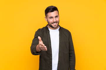 Man over isolated yellow background handshaking after good deal