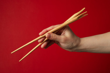 Female hand with chopsticks on red background, close up