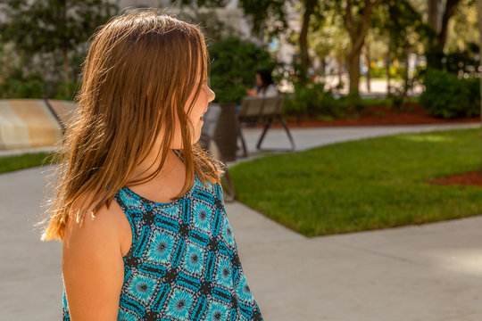 A brunette girl with sun-kissed hair looks back at her mother. Mom focuses on texting while her child smiles with joy playing at the park.