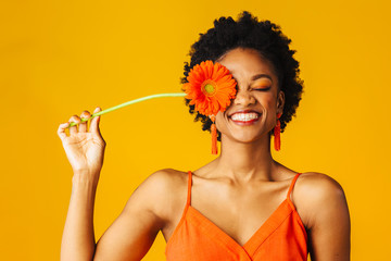 Portrait of a happy young woman holding orange Gerbera daisy covering her eye with eyes closed - Powered by Adobe