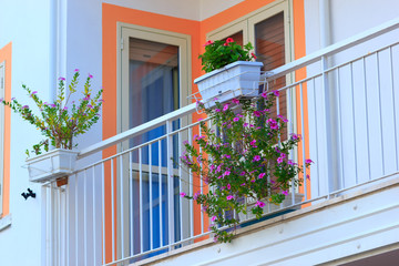 Floral balcony decoration of modern building or hotel in Italy. Blossom flowers in pot on facade.