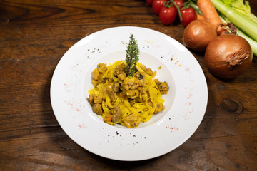 closeup of a plate of fresh tagliatelle with hare ragout with thyme branch for decoration, with the background of a tavern table with the various ingredients