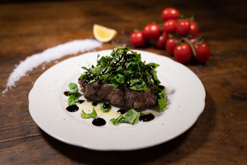 Grilled Beef fillet with fresh arugula and drops of Balsamic Vinegar on a porcelain plate typical of an old tavern