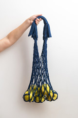 A string bag, a wicker bag made of rope with apples in women's hands on a white background.
