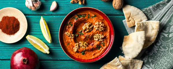 Roasted red bell pepper spread - muhammara - in a red bowl with various ingredients