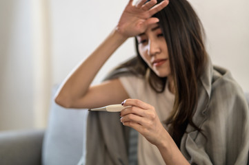 Young Asian woman have a cold and high fever while checking body temperature by using digital thermometer. Focus close up on thermometer.