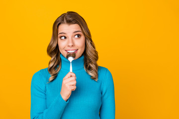 Photo of attractive charming curly lady hold metal spoon in mouth look tempting empty space dream of tasty food dinner wear blue turtleneck isolated bright shine yellow color background
