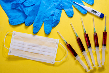 thermometer electronic indicator/display shows 39.4 degrees centigrade 39.4° C, blue nitrile gloves,surgical gloves, blood in syringes and surgical mask on the yellow background