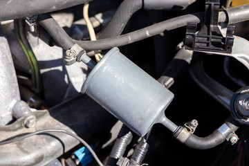 Fuel filter installed in a car with a fuel line connected to it under the open hood. Filter element in the fuel line that traps particles of dirt and rust from the gasoline. Closeup view