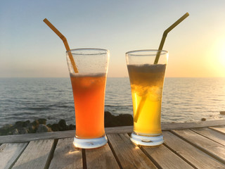 Frozen cocktail glasses with straws on wooden table over sea sunset