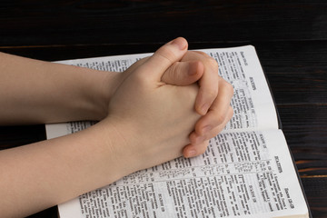 Fototapeta premium hands praying with a bible in a dark over wooden table