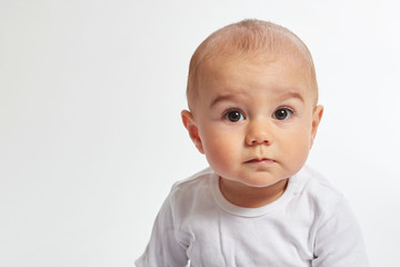 A baby boy looks into camera wearing a white shirt on a white background