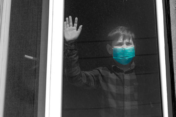 A boy in a medical mask looks out the window.