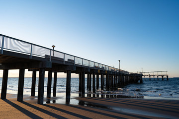 Obraz premium Sunrise over Atlantic Ocean with blue clear sky, blue ocean, wooden pier, birds flying over sunrise red sky beams 