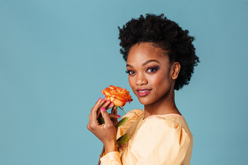 Portrait of a beautiful young woman holding yellow orange rose with pink manicure fingernails, isolated on blue background