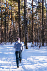A man runs on a snowy road in a mixed forest on a sunny day.
