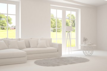 Fototapeta premium White living room with sofa and summer landscape in window. Scandinavian interior design. 3D illustration