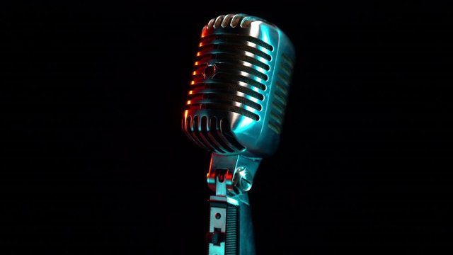 Retro microphone rotating on black background with teal orange light