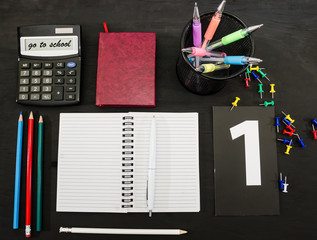 multi-colored pens, notebook, book and pencils on a black table. Education concept. View from above.