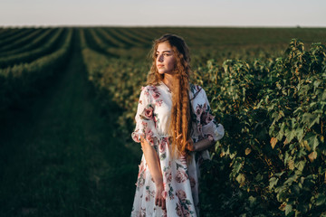 beautiful woman with long curly hair and freckles face on currant field background. Girl in a light dress walks in the summer sunny day