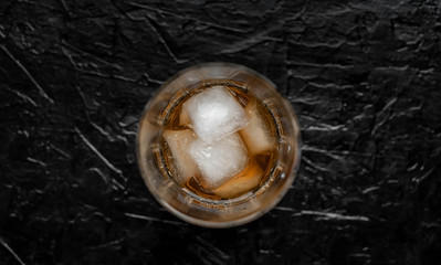 
glass of whiskey with ice on a black stone background with copy space for your text.