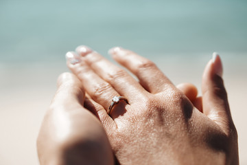 Fresh engaged couple enjoying a romantic engagement day on the beach during a sunny day. Close up on her ring.