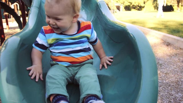 Front view of toddler joyfully sliding down playground slide summer afternoon