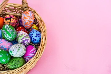 THe painted colorful Easter egg in the basket on the pink background copyspace to celebrate the traditional festival