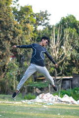 A boy wearing sunglass jumping from ground and freezes in air wearing black t-shirt and white pant.