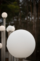 Large round lamps on a city street. Modern white lights on a metal bar. Stylish lights in the city center. Led