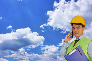 Young engineer with helmet  and clipboard, speaking on mobile phone