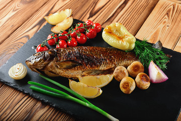 Grilled fish with vegetables, mushrooms and herbs on a black slate plate. Close up.