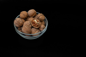 Glass bowl with walnuts in peel on a black background