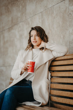 Beautiful young girl sitting and enjoing coffee .sitting on a bench in the city