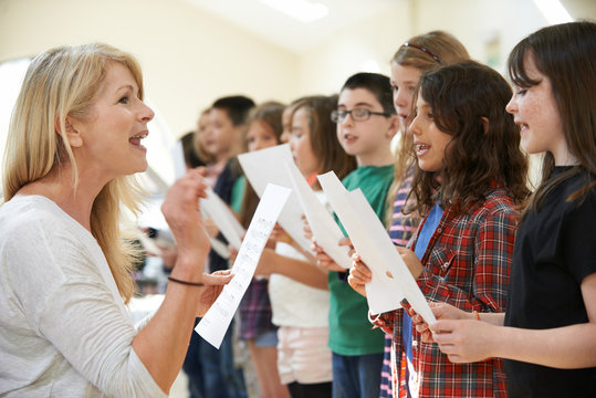 Children In Singing Group Being Encouraged By Teacher At Stage School