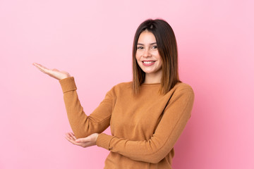 Young woman over isolated pink background extending hands to the side for inviting to come