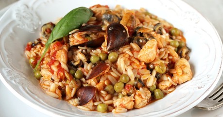 paella from orzo pasta with mussels, seashells and chicken. Seafood paella, traditional spanish dish. Paella on rustic black wooden table. Top view
