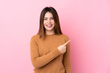 Young woman over isolated pink background surprised and pointing side