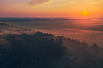 Beautiful red dawn on a summer morning with fog in the forest and fields. View from above