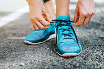 Running blue shoes and runner woman tying laces run in forest road. 