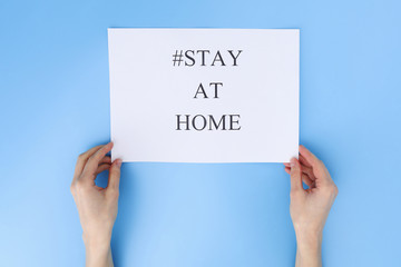 stay at home concept. woman hand holding paper with words stay at home isolated on blue background. Coronavirus, COVID-19, self-quarantine, isolation
