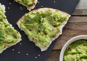 fresh guacamole sauce with peas microgreen and sesame seeds on toasted tortillas on a black slate...